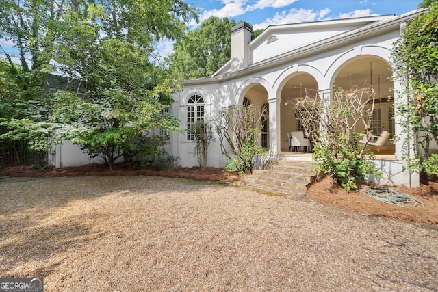 rear view of property featuring stucco siding, a chimney, and a porch