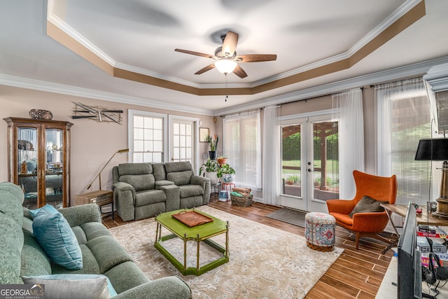 living room with a raised ceiling, french doors, ceiling fan, wood finished floors, and ornamental molding