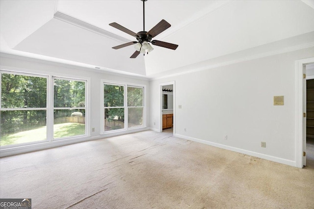 unfurnished living room with a raised ceiling, light colored carpet, a ceiling fan, baseboards, and crown molding