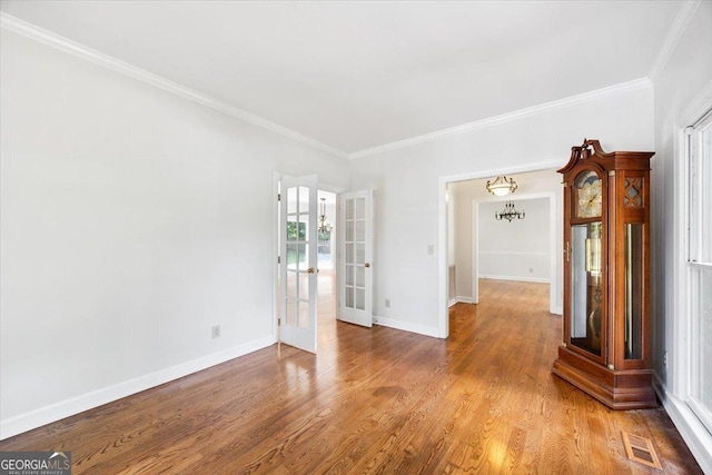 empty room featuring french doors, crown molding, wood finished floors, and baseboards