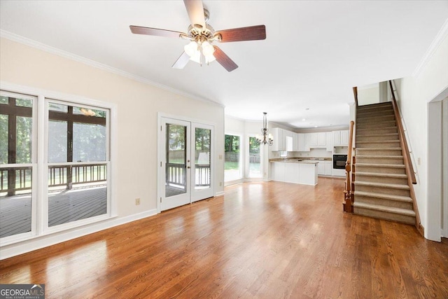 unfurnished living room with ornamental molding, a chandelier, stairs, wood finished floors, and a ceiling fan