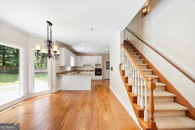 kitchen with oven, white cabinets, crown molding, light wood-type flooring, and a chandelier