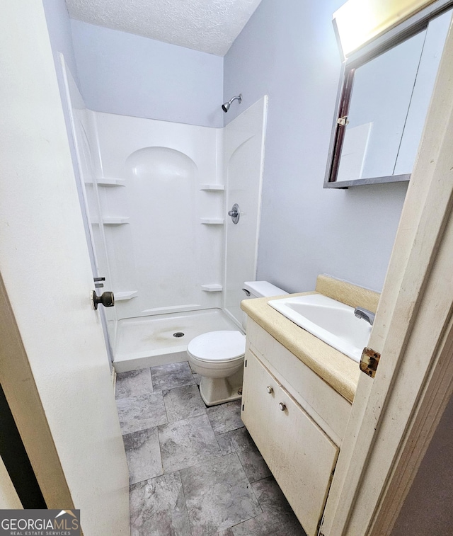 bathroom with stone finish floors, a shower stall, toilet, vanity, and a textured ceiling