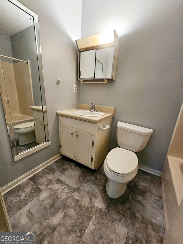 full bath featuring toilet, vanity, stone finish flooring, and baseboards