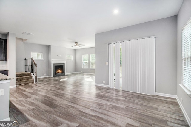 2769 Morgan Spring Trl, Buford, GA 30519 - unfurnished living room with stairway, wood finished floors, ceiling fan, a warm lit fireplace, and baseboards