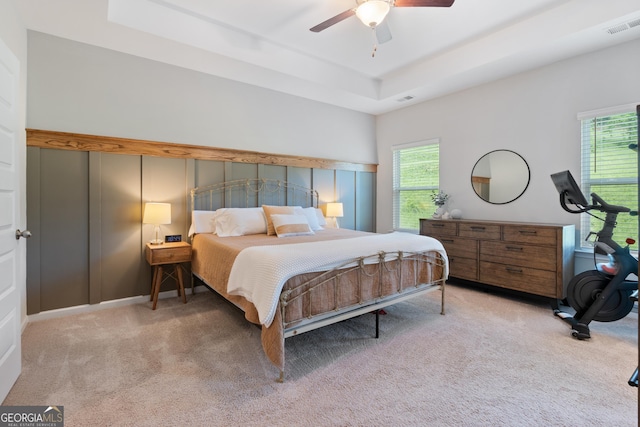 carpeted bedroom with multiple windows, a raised ceiling, and ceiling fan