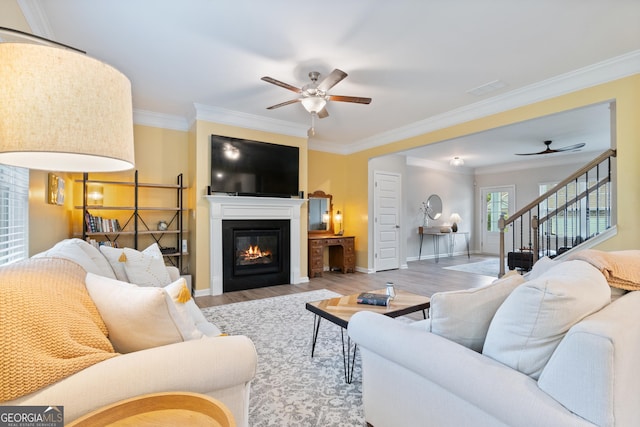 living area featuring ceiling fan, wood finished floors, baseboards, stairs, and ornamental molding