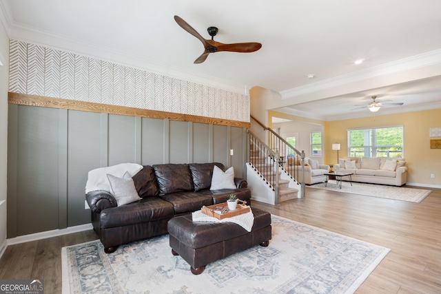 living room featuring ceiling fan, stairway, ornamental molding, wood finished floors, and a decorative wall