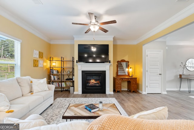 living room with ceiling fan, ornamental molding, wood finished floors, a glass covered fireplace, and baseboards
