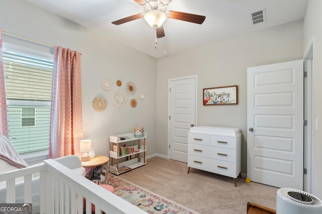 bedroom featuring light carpet, a crib, a ceiling fan, and baseboards