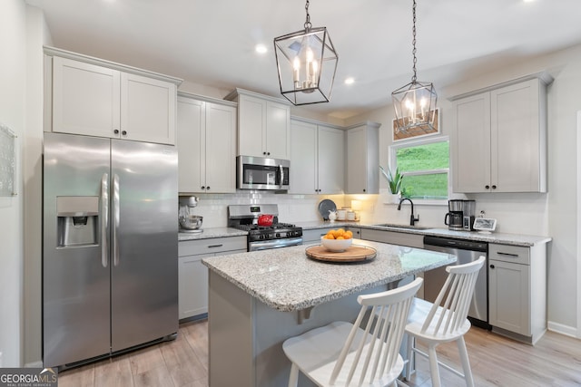 kitchen with appliances with stainless steel finishes, a sink, a chandelier, decorative backsplash, and light wood-style floors