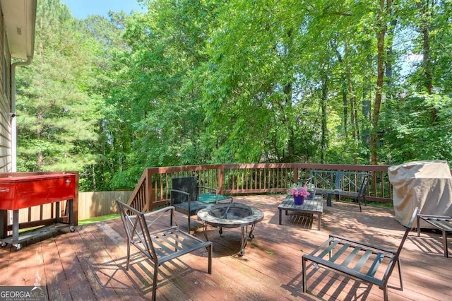 wooden deck featuring an outdoor fire pit, area for grilling, and a forest view