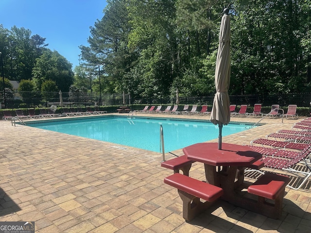 community pool featuring a patio, fence, and view of scattered trees