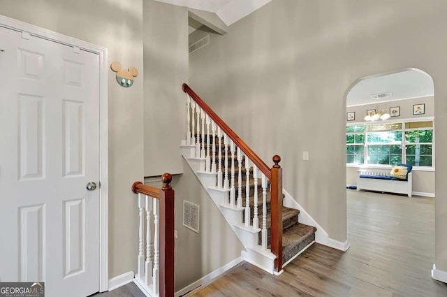 stairs with wood finished floors, arched walkways, and baseboards