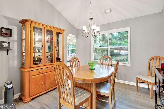 dining room featuring a chandelier, light wood-style flooring, lofted ceiling, baseboards, and arched walkways