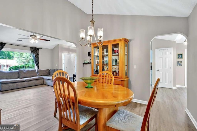 dining room with arched walkways, light wood-style floors, a ceiling fan, a chandelier, and vaulted ceiling
