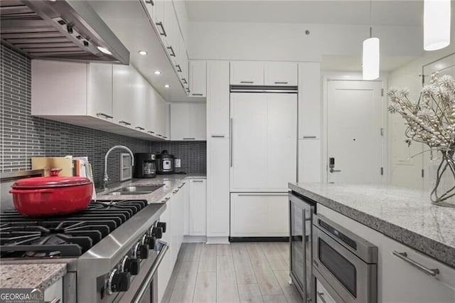 1820 Peachtree St Unit 311, Atlanta, GA 30309 - kitchen featuring a sink, built in appliances, wall chimney exhaust hood, white cabinetry, and backsplash