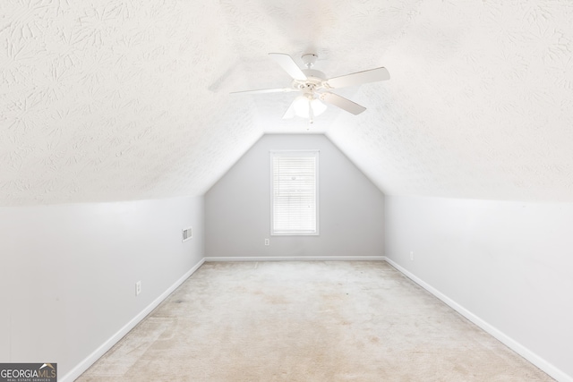 additional living space featuring a textured ceiling, vaulted ceiling, baseboards, ceiling fan, and carpet