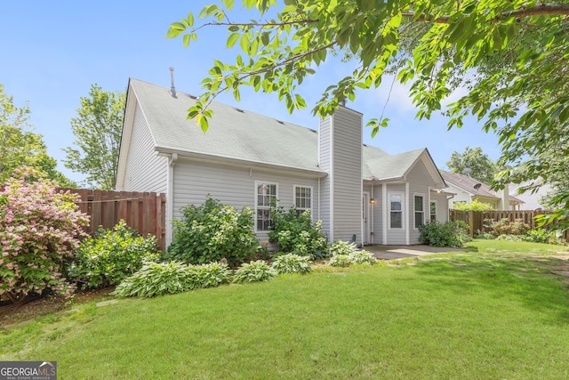 back of house with a chimney, a patio, and a shingled roof