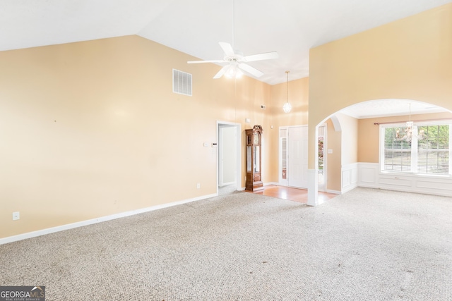 unfurnished living room with arched walkways, carpet floors, high vaulted ceiling, ceiling fan, and wainscoting