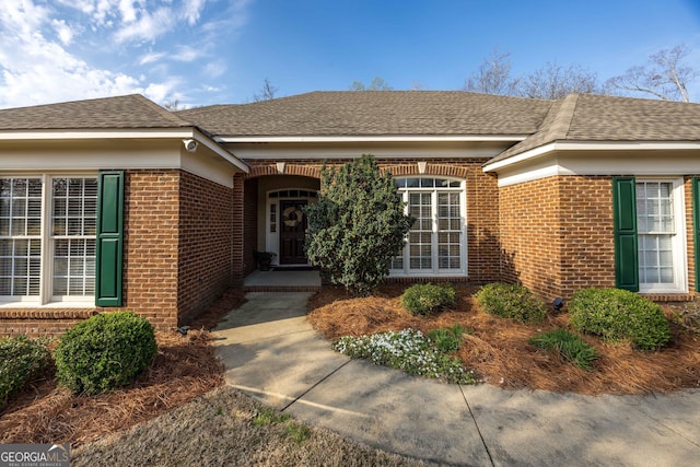 entrance to property featuring brick siding and roof with shingles
