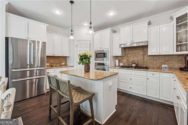 kitchen featuring appliances with stainless steel finishes, under cabinet range hood, a center island, white cabinetry, and dark wood finished floors