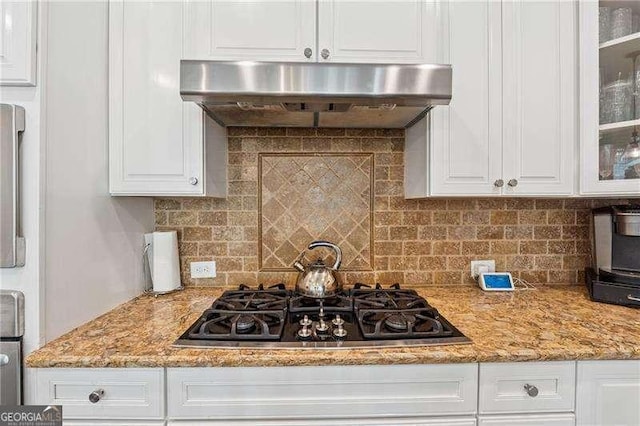 kitchen featuring black gas stovetop, under cabinet range hood, white cabinets, glass insert cabinets, and backsplash