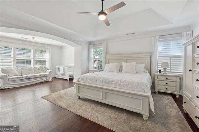 bedroom featuring a tray ceiling, multiple windows, dark wood finished floors, arched walkways, and crown molding
