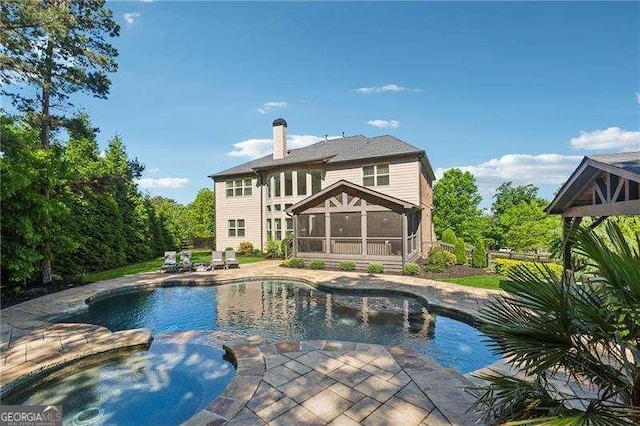 rear view of house featuring a sunroom, a chimney, a patio area, and a pool with connected hot tub