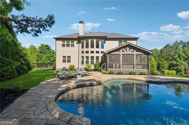 back of house with a sunroom, a chimney, a patio area, and an outdoor pool