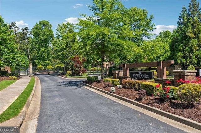 view of asphalt road with curbs, a gated entry, a gate, and sidewalks