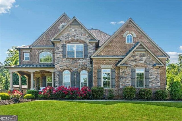 view of front facade featuring a front lawn, stone siding, covered porch, and brick siding