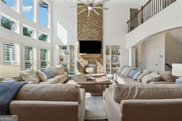 living area featuring a towering ceiling, ceiling fan, arched walkways, a stone fireplace, and built in features
