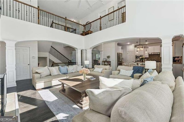 living area with a high ceiling, decorative columns, arched walkways, dark wood finished floors, and stairs