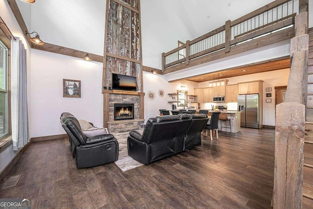living room with a stone fireplace, dark wood finished floors, a high ceiling, and baseboards