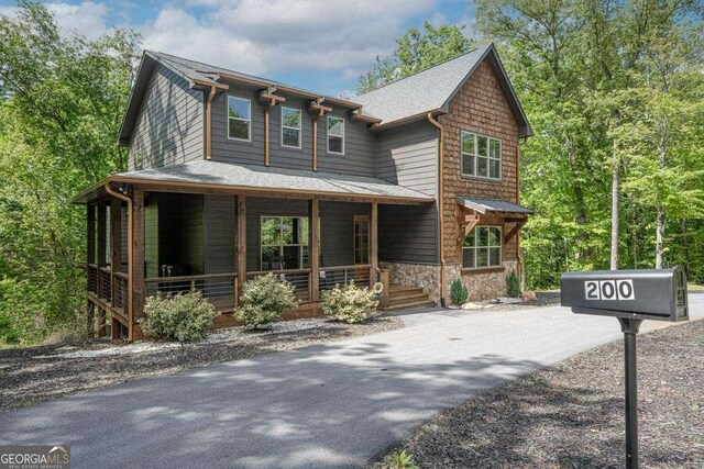 view of front of home featuring covered porch, stone siding, and asphalt driveway