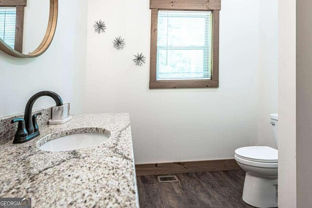 bathroom with toilet, healthy amount of natural light, wood finished floors, and baseboards
