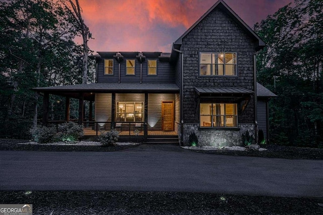 back of property featuring stone siding, covered porch, and a standing seam roof