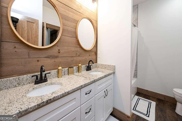 full bath with double vanity, toilet, wood walls, baseboards, and shower / bath combination with curtain