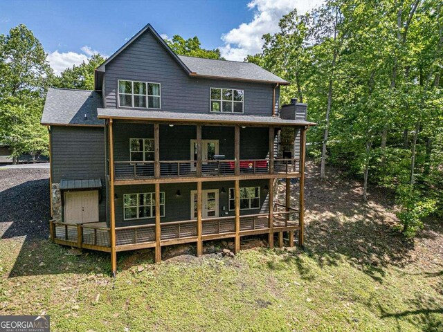 back of property featuring a deck, a lawn, and roof with shingles