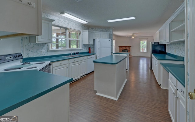 kitchen featuring white appliances, a center island, ceiling fan, a fireplace, and dark wood-style floors