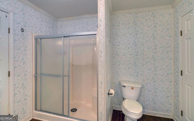 bathroom with a shower stall, a textured ceiling, crown molding, toilet, and wallpapered walls