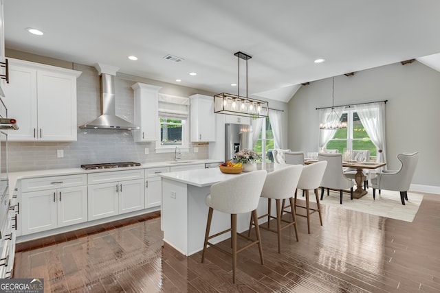 kitchen featuring wall chimney range hood, appliances with stainless steel finishes, a sink, a center island, and a kitchen bar