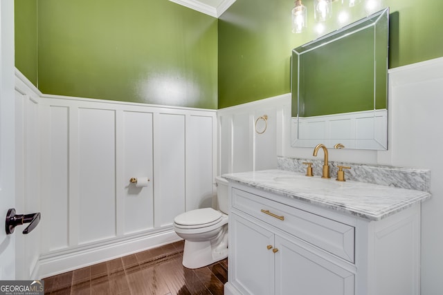 bathroom featuring a decorative wall, toilet, a wainscoted wall, vanity, and wood finished floors