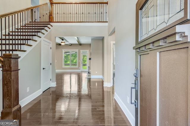 foyer entrance featuring baseboards, stairs, beam ceiling, a high ceiling, and wood finished floors