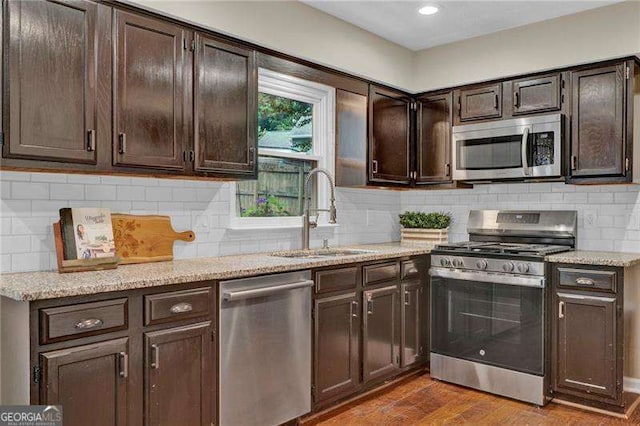 kitchen featuring stainless steel appliances, a sink, dark wood finished floors, dark brown cabinets, and backsplash