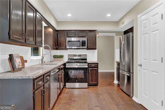 kitchen with appliances with stainless steel finishes, a sink, wood finished floors, dark brown cabinets, and backsplash