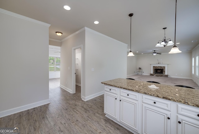 kitchen with ceiling fan, a brick fireplace, ornamental molding, baseboards, and light stone counters