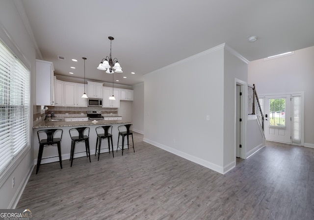 kitchen featuring appliances with stainless steel finishes, a chandelier, a peninsula, decorative backsplash, and wood finished floors