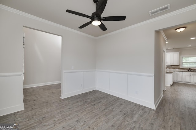 empty room featuring ornamental molding, wood finished floors, ceiling fan, a sink, and wainscoting